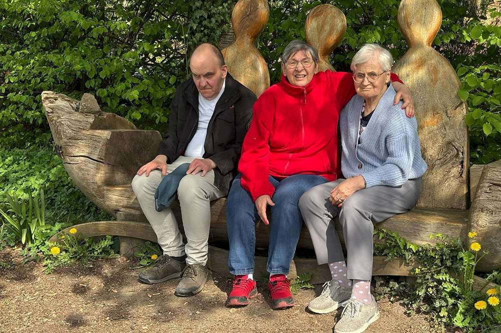 Bild zeigt drei ältere Personen auf einer Holzbank.