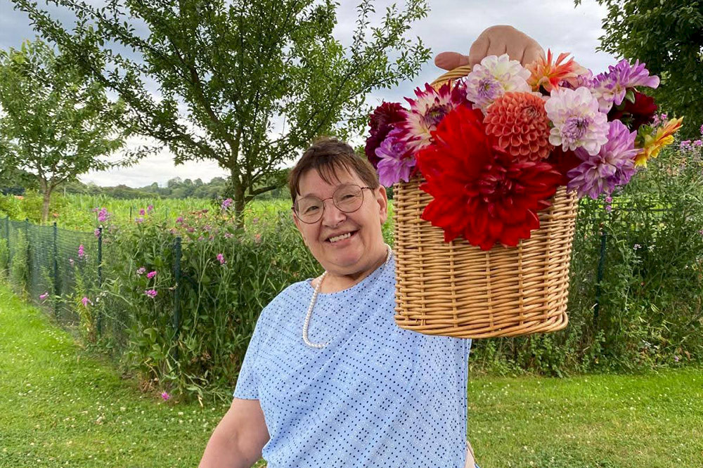 Bild zeigt eine Person mit einem großen Blumenkorb.